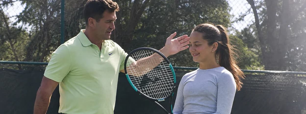 Coach greeting a young tennis player on court